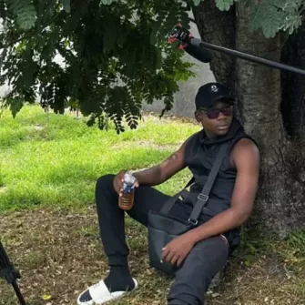 Un jeune homme assis sous un arbre. On aperçoit à gauche une caméra et à droite un micro.